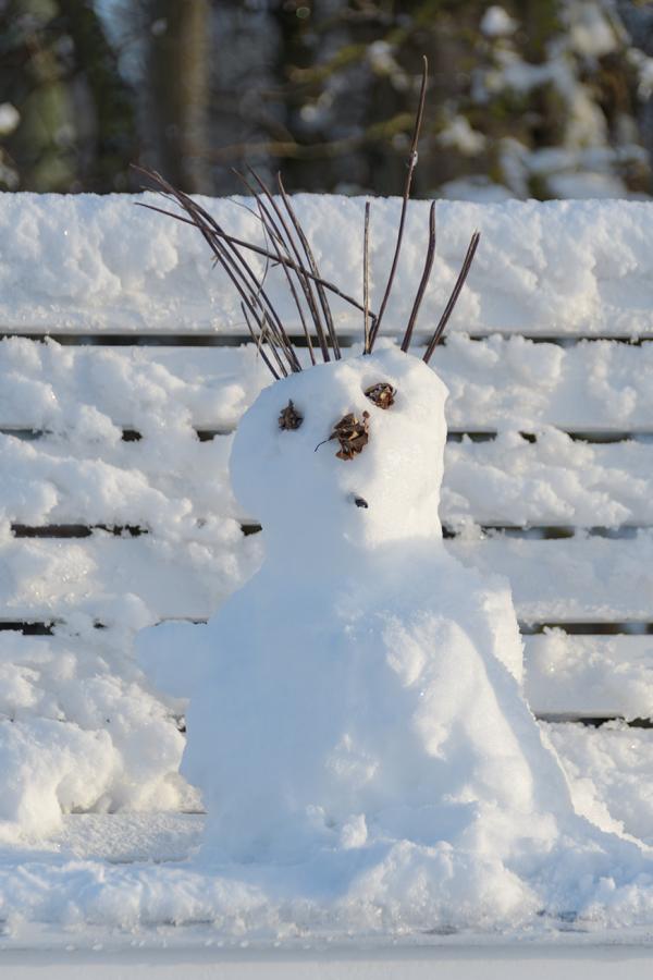 Porrait eines lleinen Schneemannes auf Parkbank im Winter